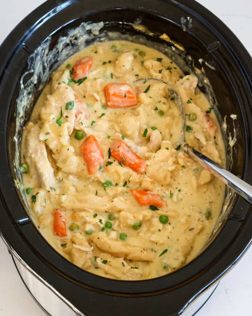 A crockpot full of chicken and dumplings with carrots and peas.