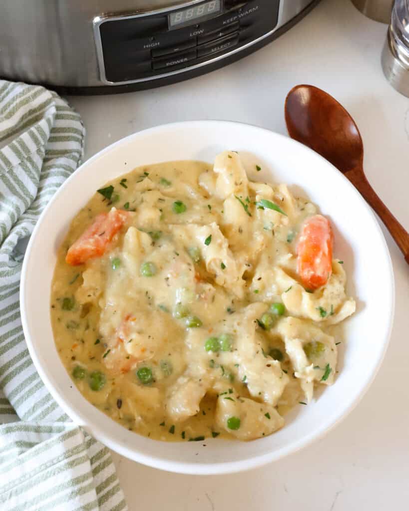 A single serving bowl full of crock pot chicken and dumplings with a wooden spoon and salt and pepper shaker in the background. 