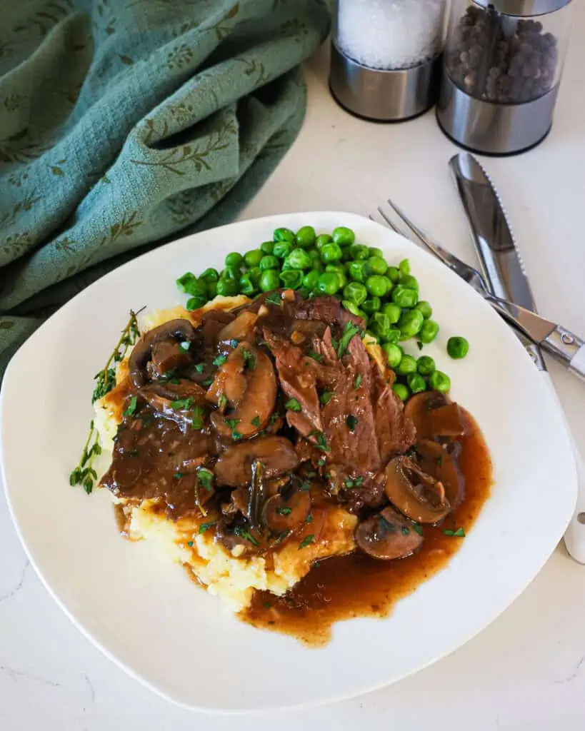 Round steak and gravy over mashed potatoes with a side of sweet peas. 