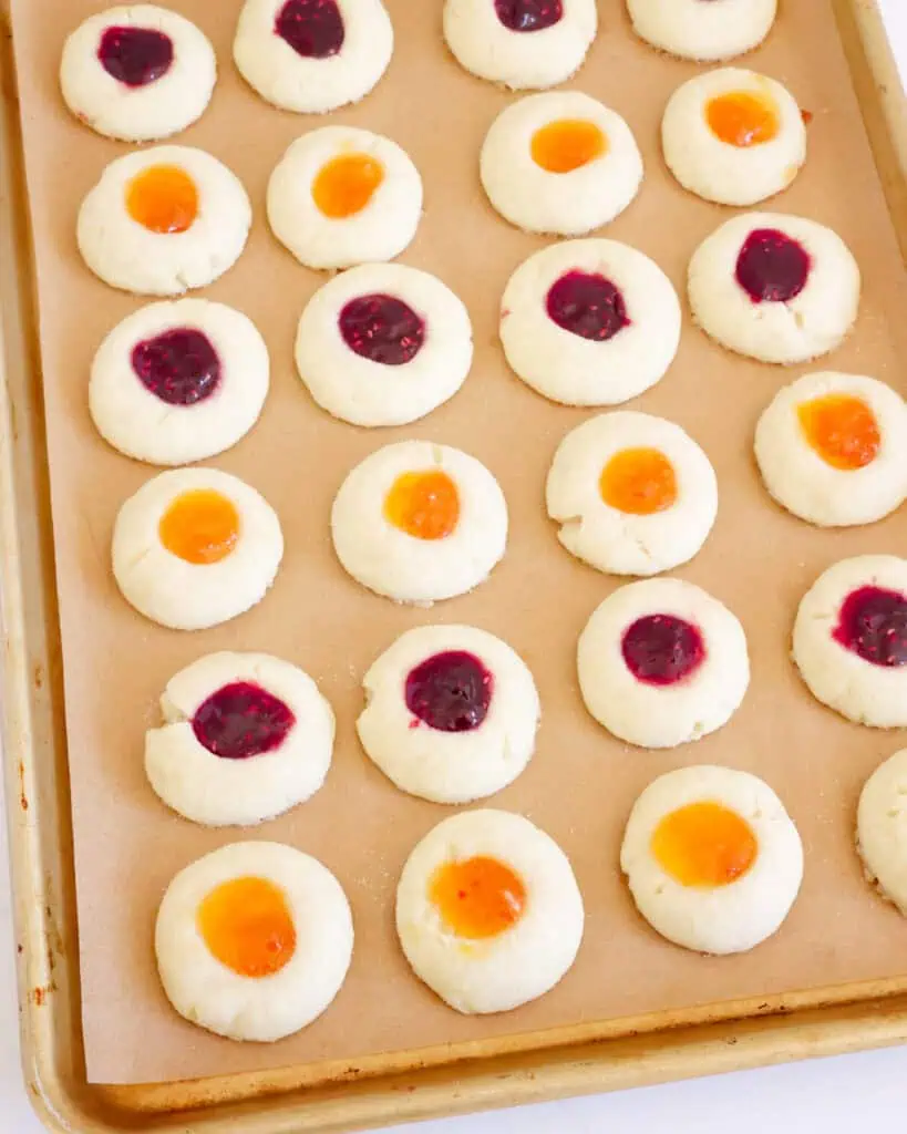 Jam filled thumbprint cookies on a parchment covered bsking sheet. 