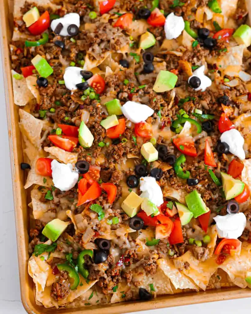 A large baking sheet full nacchos with black olives, tomatoes, and avocadoes. 