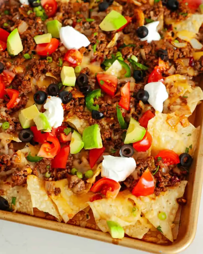 A close up view of nachos on a baking sheet. 