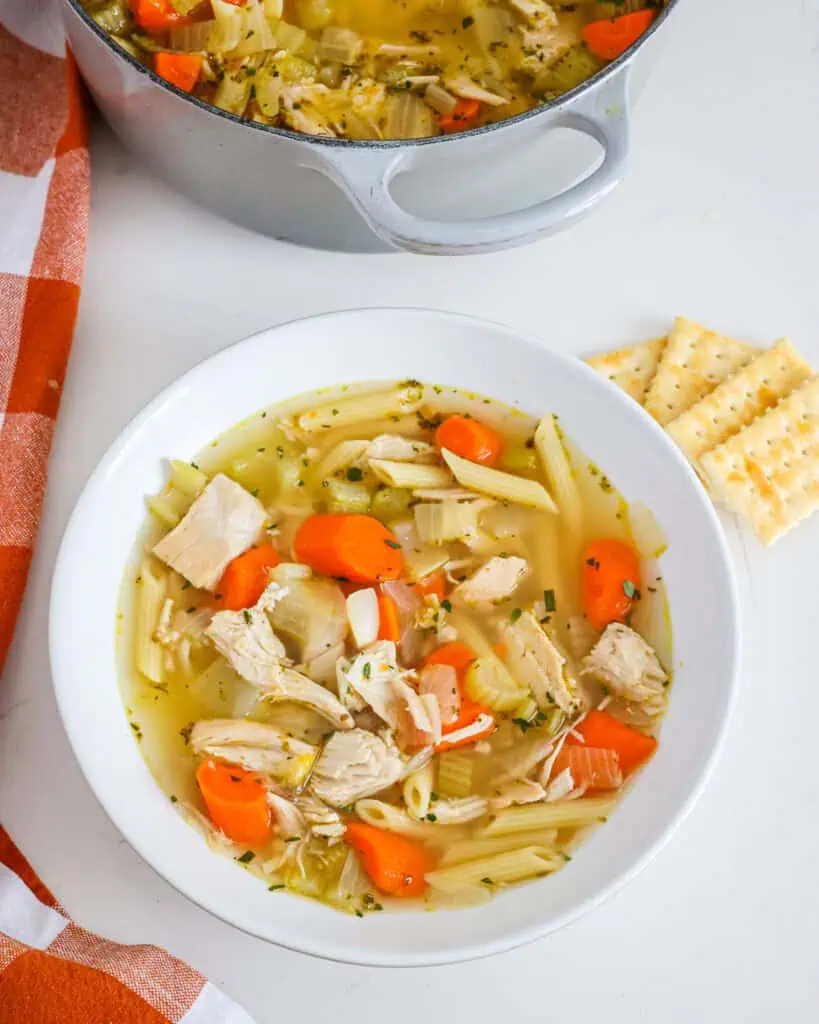 A bowl full of turkey soup with crackers on the side and the Dutch oven full of turkey soup in the background. 