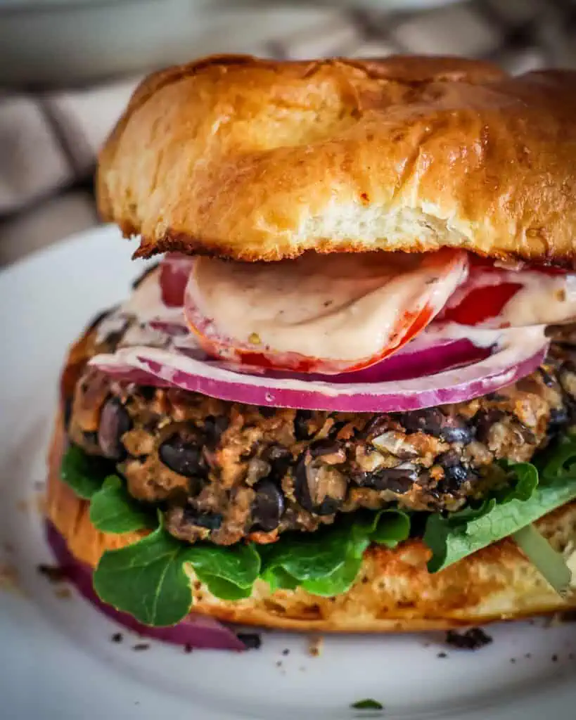 A close up view of a black bean burger with lettuce, tomato, and ed onion on a toasted bun. 