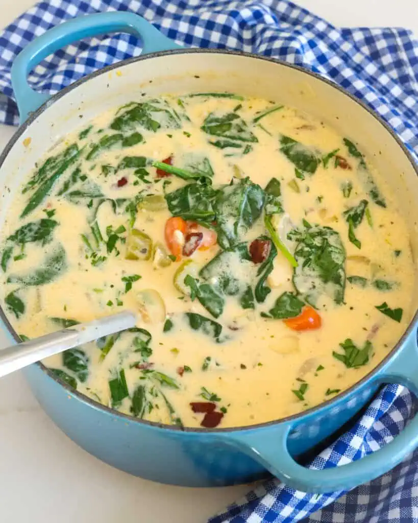 A Dutch oven full of crack chicken soup with bacon, onions, carrots, tender chicken, and ranch seasoning in a super creamy cheesy broth with spinach and sour cream. 