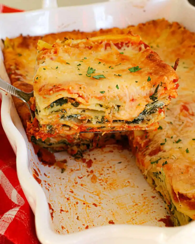 A slice of fresh baked spinach lasgna on a serving spatula over the spinach lasagna casserole. 