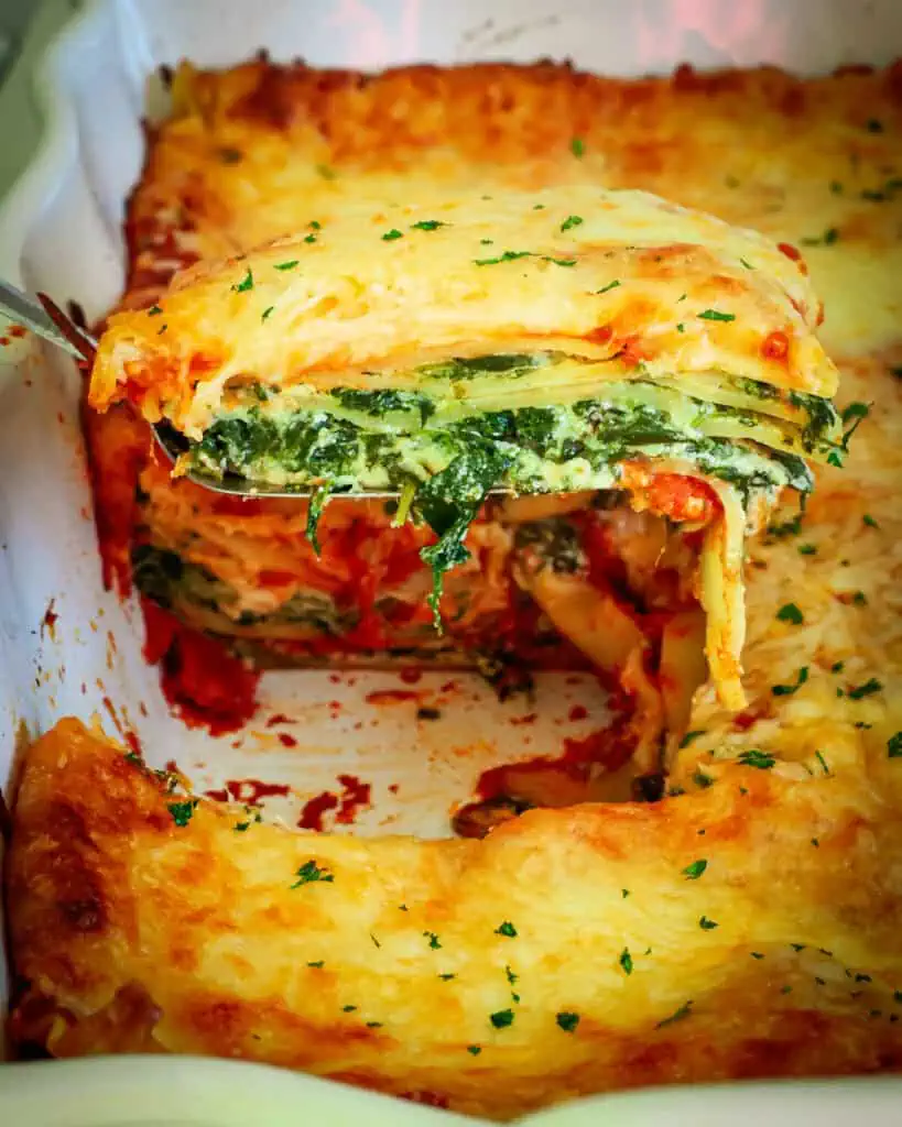 A slice of spinach lasagna on a serving spatula over the rest of the lasagna casserole. 