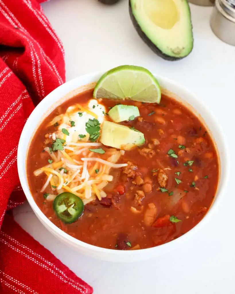 Turkey chili in a single serving bowl with jalapeno rings, shredded cheddar and Monterey Jack, and sour cream. 