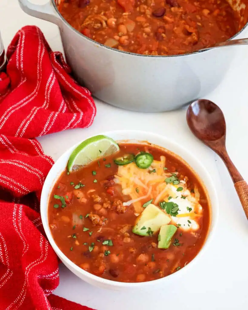 Overhead view of turkey chili with Johnny cakes, a wooden spoon, and a green kitchen towel. 