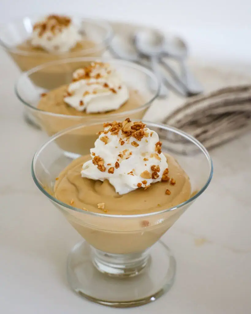 Three sundae dishes filled with butterscotch pudding and topped with whipped cream and granola. 