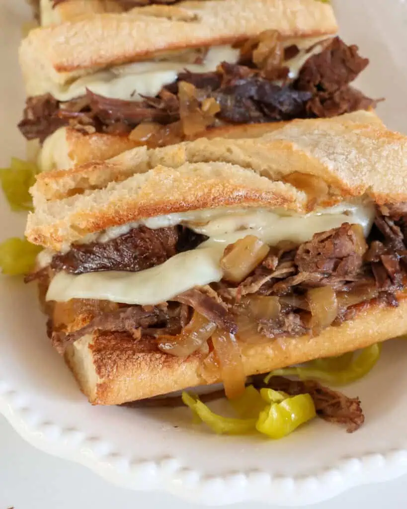 A close up view of French dip sandwiches with slow cooked beef, onions, and Provolone cheese on toasted French bread. 