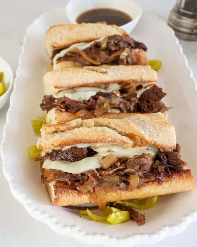 Three French dip sandwiches on a platter with au jus. 
