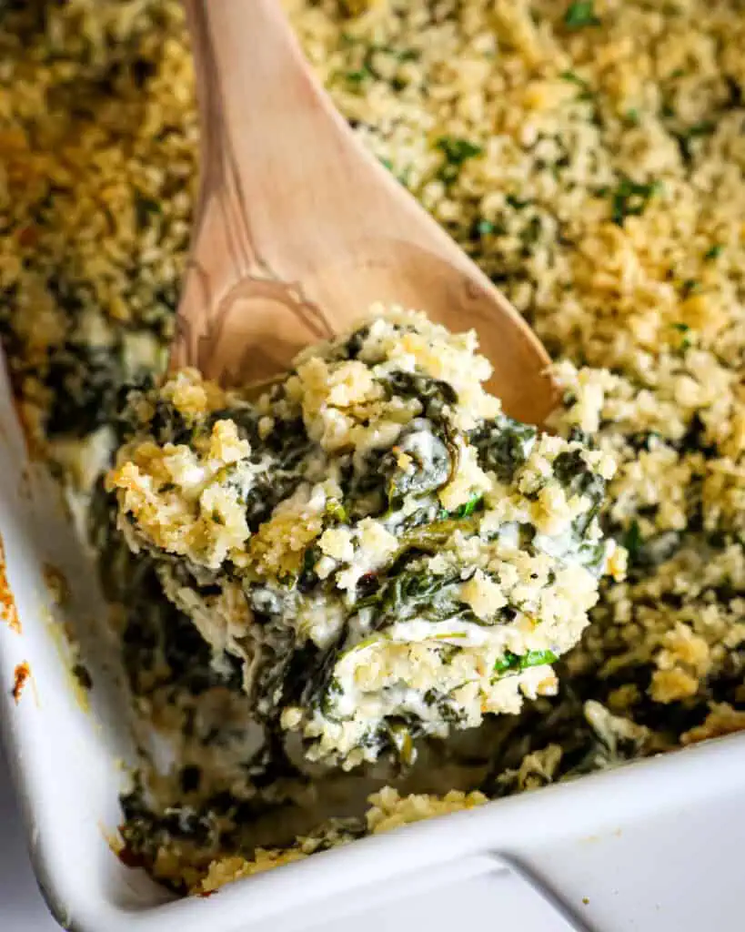 A spoon and casserole dish full of spinach casserole. 