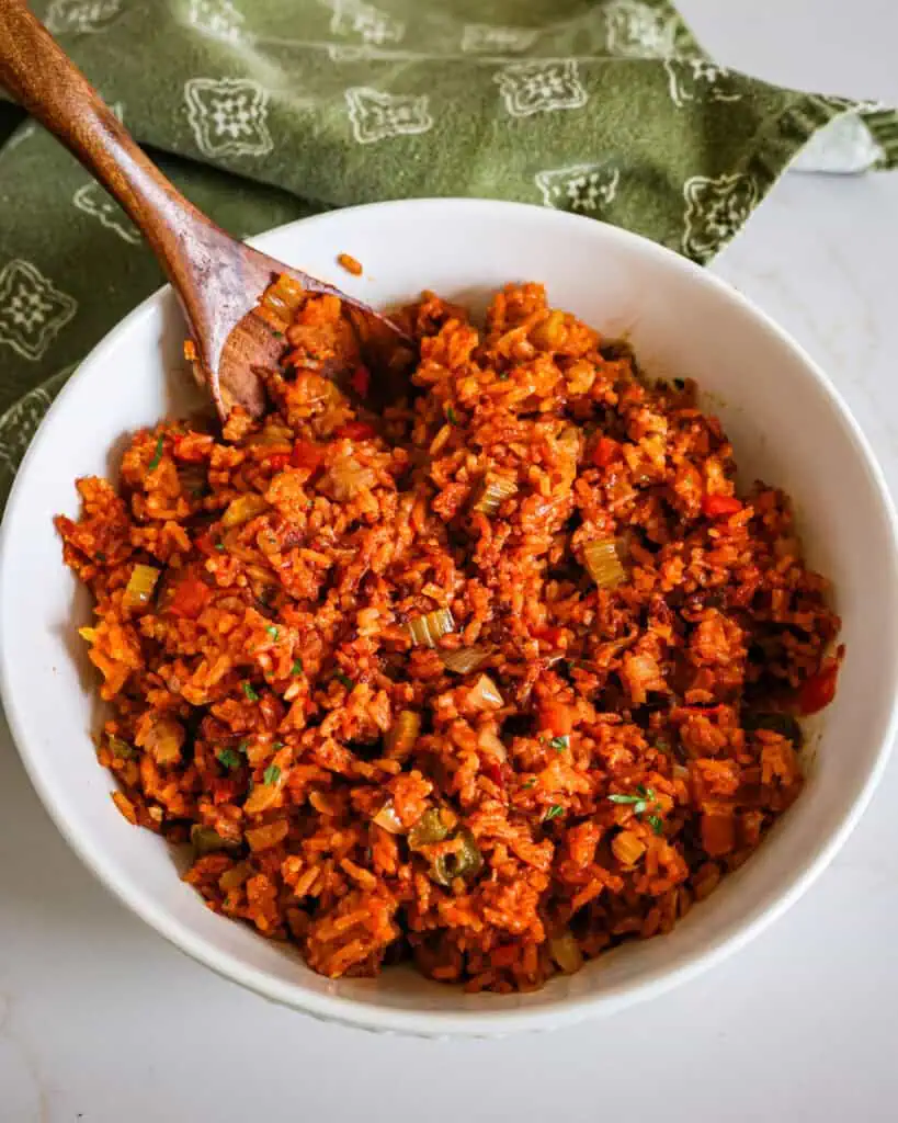 A round white serving full of Charleston red rice with a wooden serving spoon.