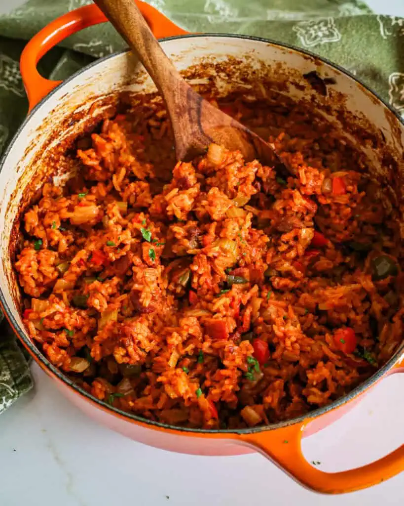 A Dutch oven full of fresh baked Charleston red rice with a wooden spoon in it. 