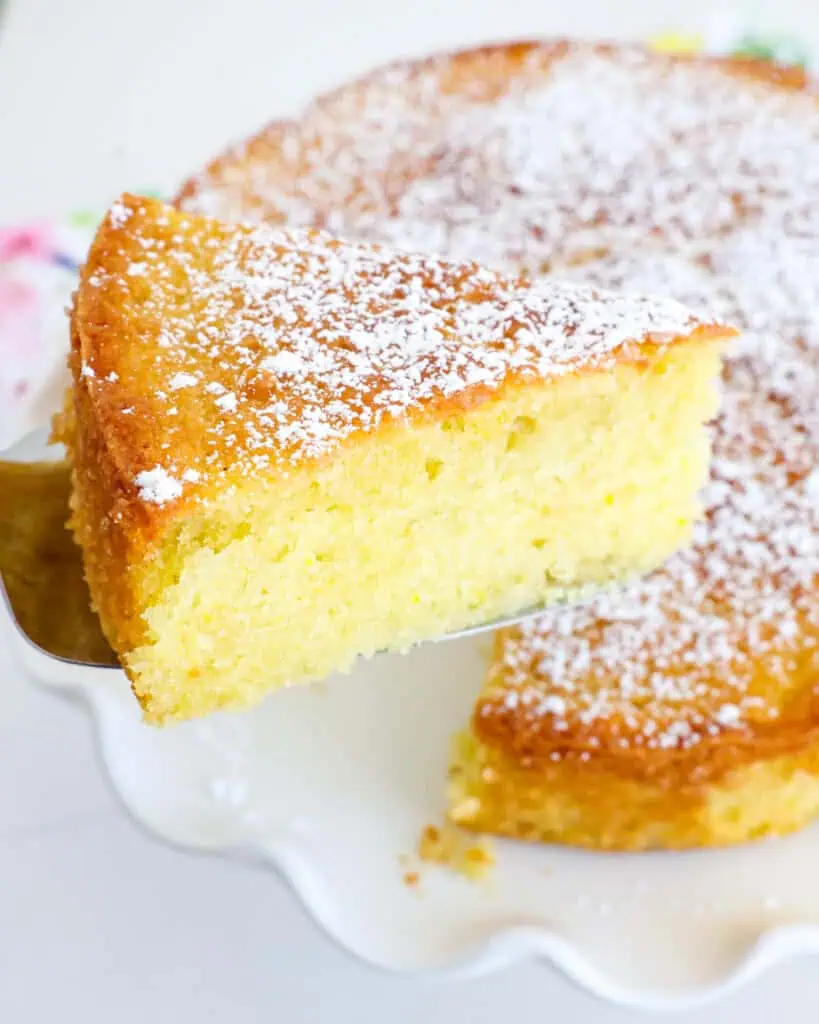 A slice of olive oil cake on a cake server over the olive oil cake. 